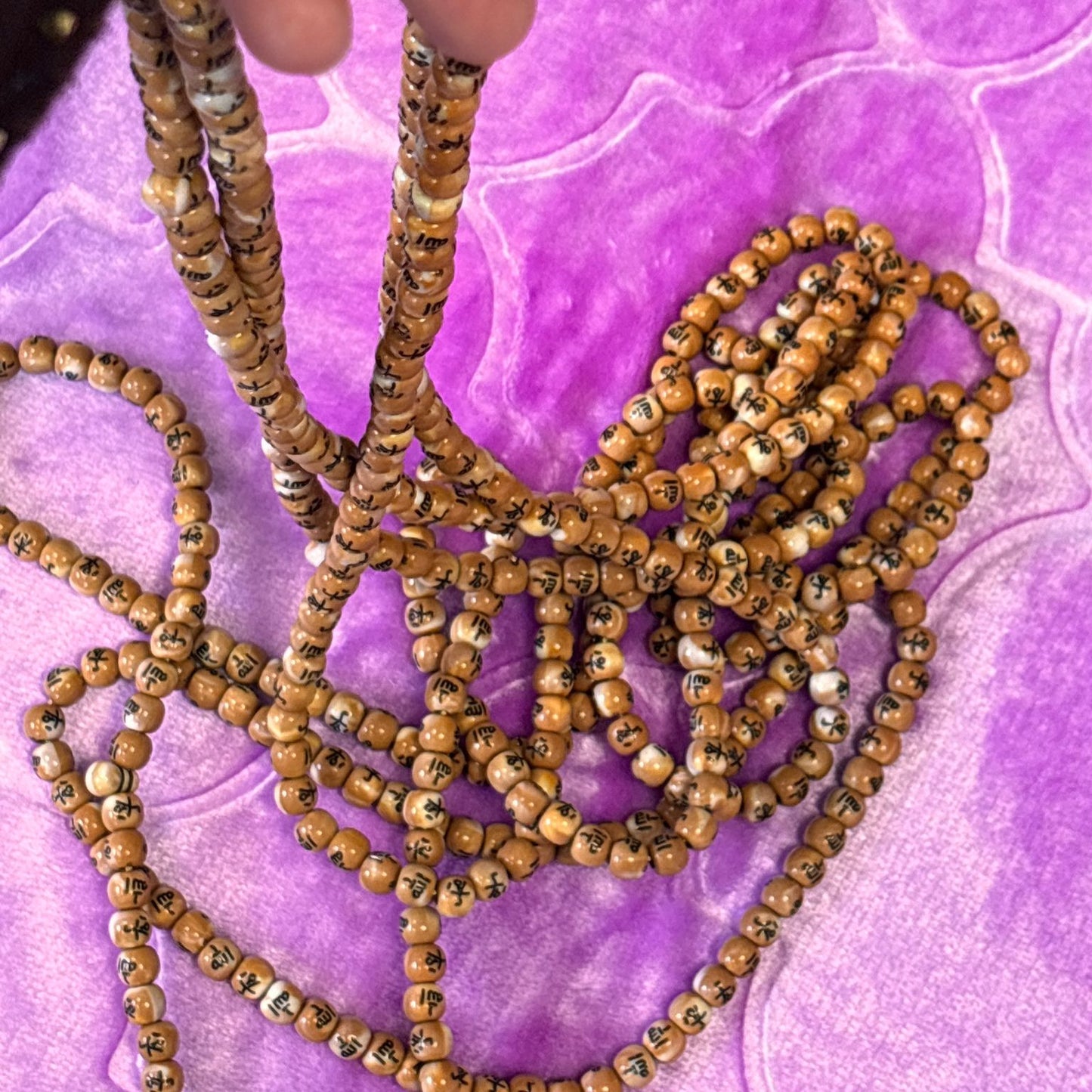 Hand holding a string of wooden beads on a purple textured surface
