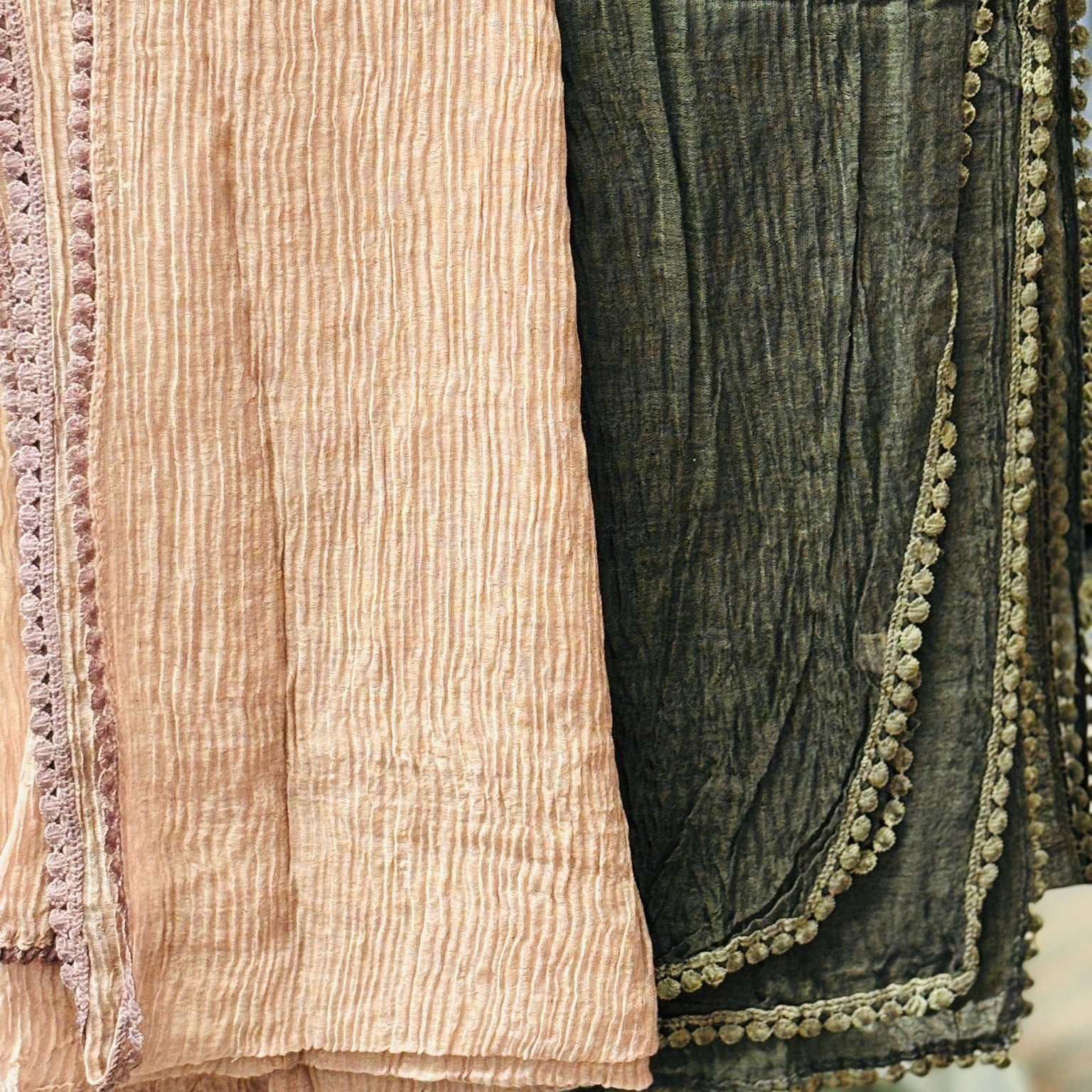 Two textured scarves, one beige and one green with decorative trim, draped over a surface.