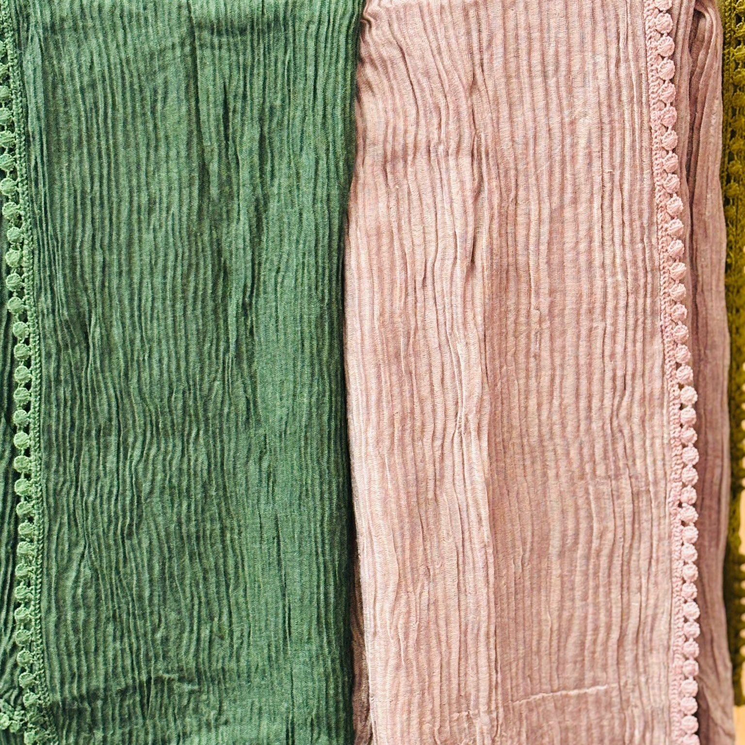 Two textured scarves, one green and one pink, draped over a surface.