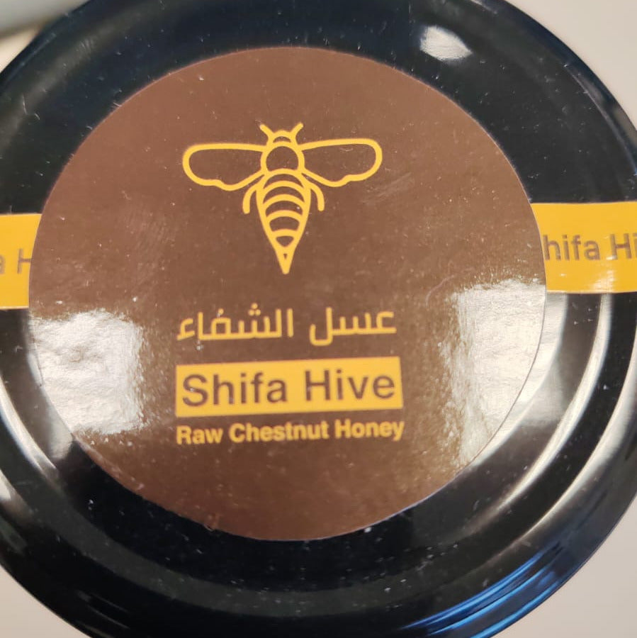 Container of Shifa Hive raw chestnut honey on a desk with a keyboard in the background