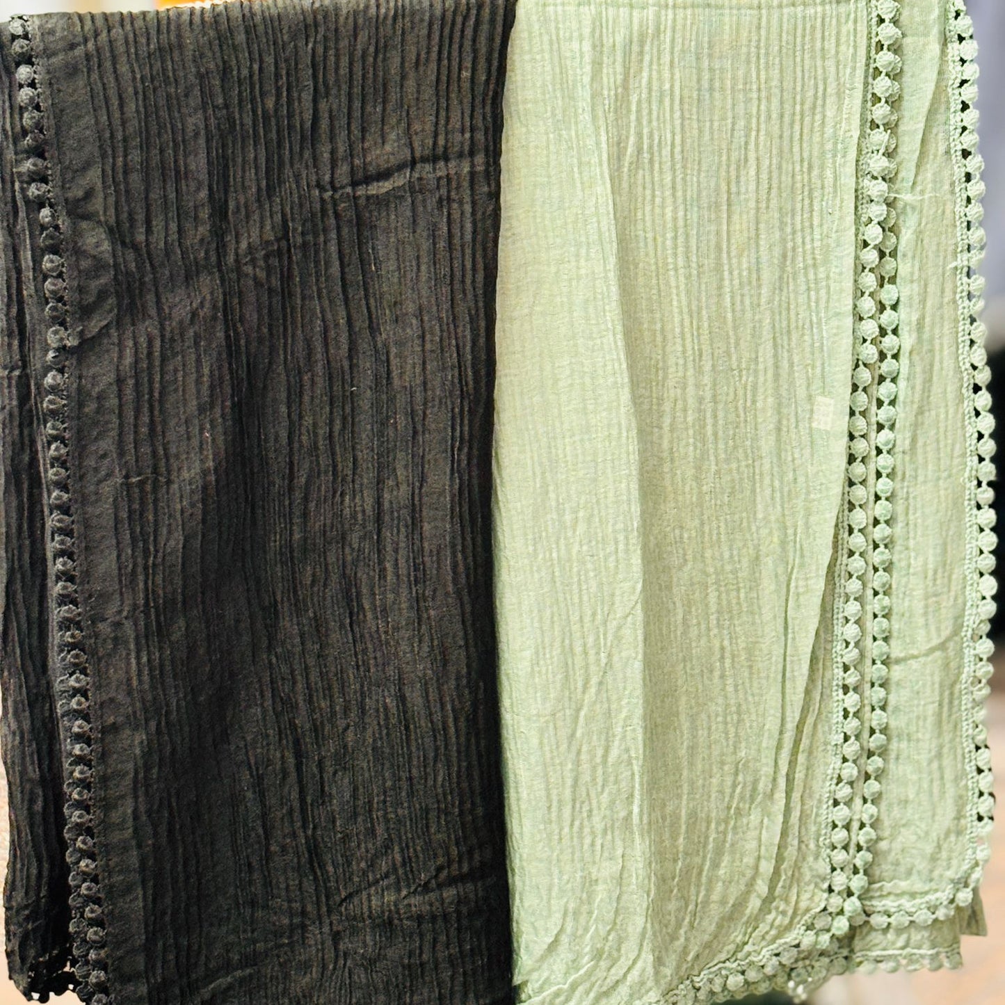 Two scarves, one black and one green with pom-pom trim, hanging on a rack.