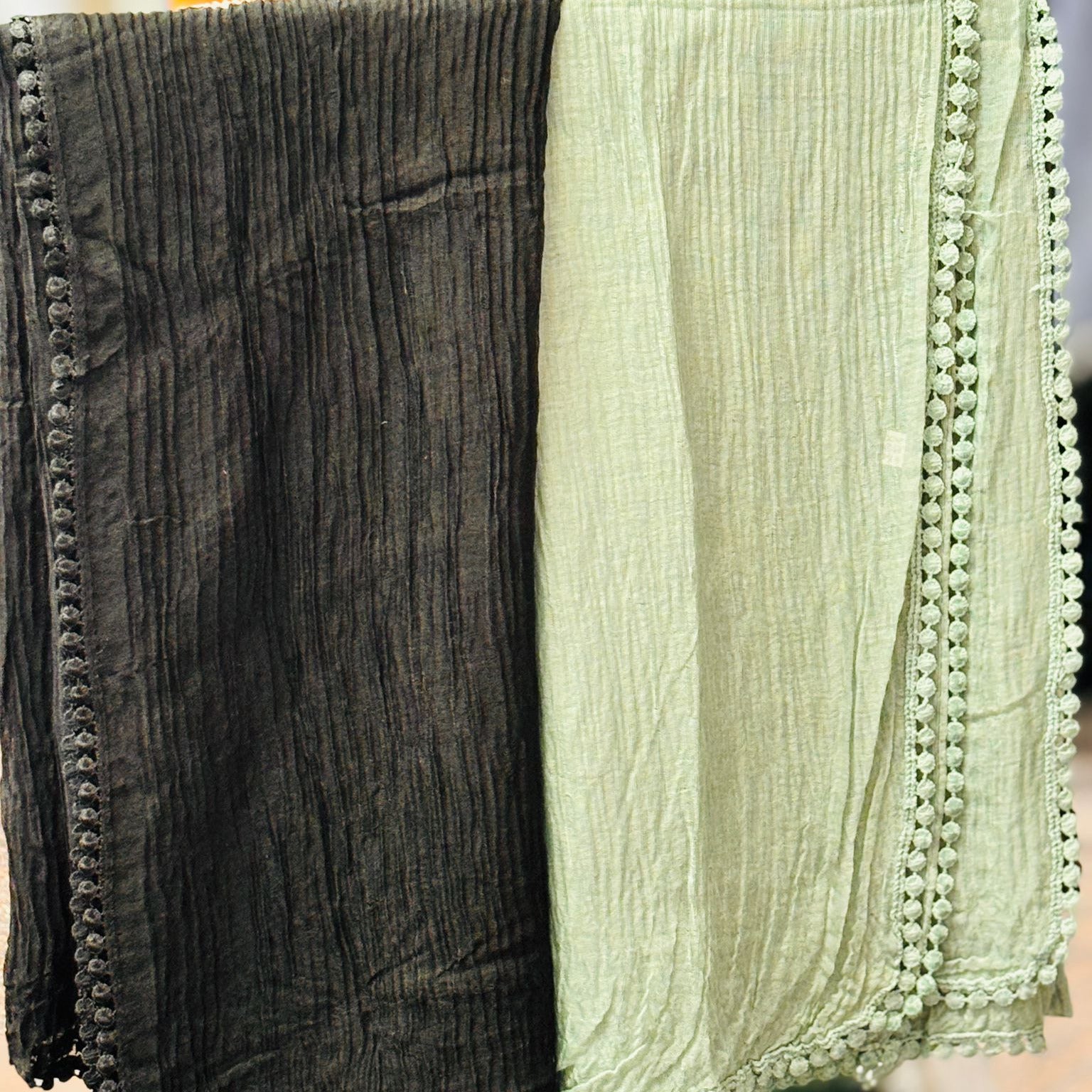 Two scarves, one black and one green with pom-pom trim, hanging on a rack.